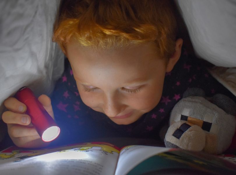 Leser i senga med lommelykt - illustrasjonsfoto