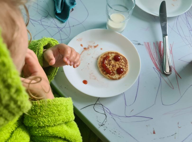 Liten pannekake med smilefjes på servert til barn med grønn morgenkåpe.