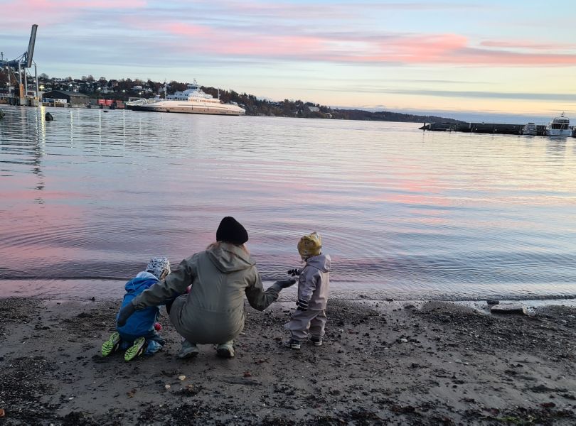 To barn på strand med en voksen. I lilla og blått vær